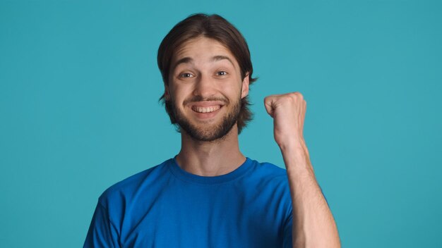 Foto homem alegre, levantando o punho comemorando o sucesso isolado em fundo azul cara se sentindo vencedor