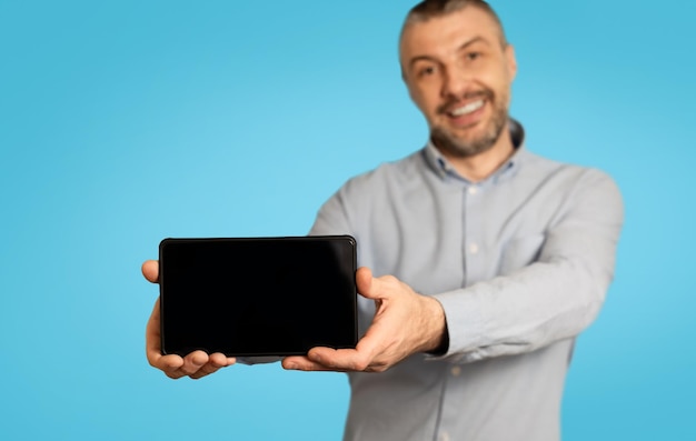 Homem alegre mostrando o celular com tela em branco fundo azul