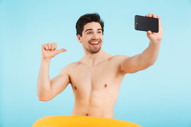 Homem alegre sem camisa, isolado, tirando uma selfie com anel inflável