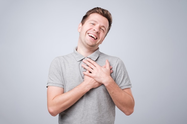 Homem alegre sorri alegremente mantém as mãos no peito Macho satisfeito feliz em receber elogios da mulher