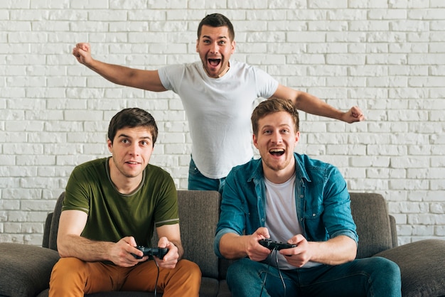 Homem alegre torcendo para os amigos jogando videogame em casa