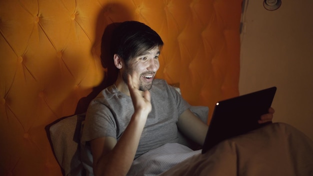 homem alegre usando computador tablet tendo chat de vídeo online enquanto estava deitado na cama em casa