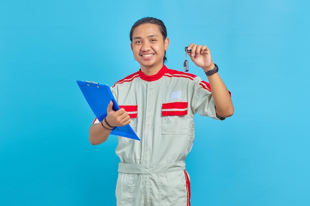 Homem alegre, vestindo uniforme de mecânico, segurando a prancheta e mostrando as chaves do veículo sobre fundo azul