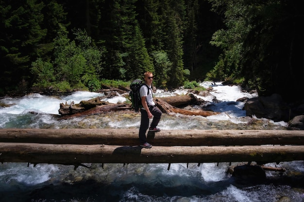 Homem alpinista caminhando atravessando o rio andando em equilíbrio no tronco de árvore caído