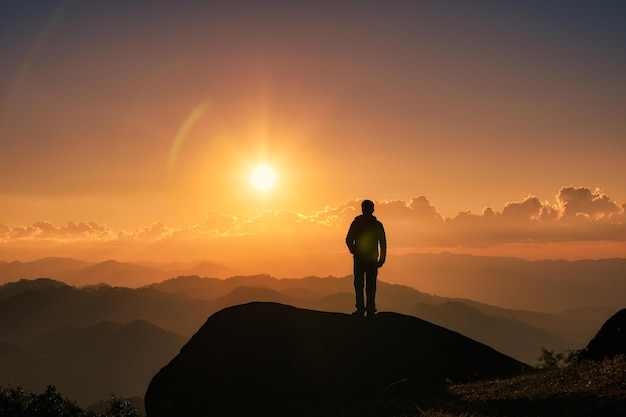 Homem alpinista de silhueta em pé no topo da montanha com o sol brilhando sobre a montanha no pôr do sol