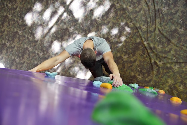Homem alpinista subindo na parede de prática de cor