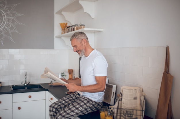 Homem alto de cabelos grisalhos lendo um jornal e parecendo interessado