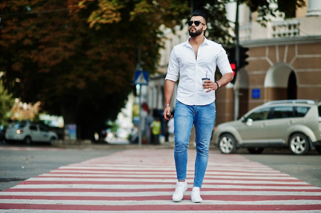 Homem alto elegante de camisa branca, calça jeans e óculos de sol, colocados na rua da cidade