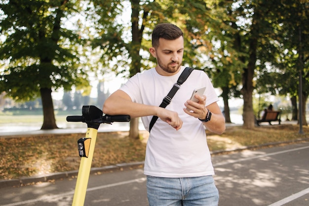 Homem amável usando telefone durante o intervalo antes de andar no escooter