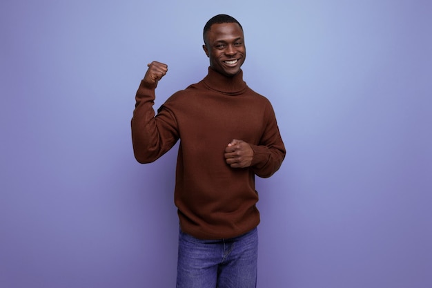 Homem americano de pele escura inteligente com corte de cabelo curto em um suéter marrom mostra sua mão em um