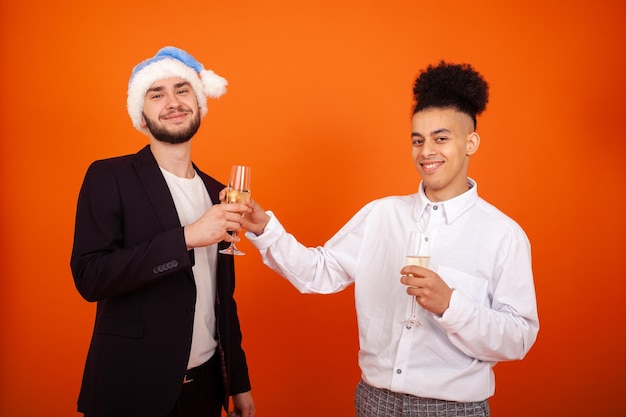Homem americano gay elegante oferecendo um copo de vinho a um homem caucasiano alegre usando um chapéu de Papai Noel