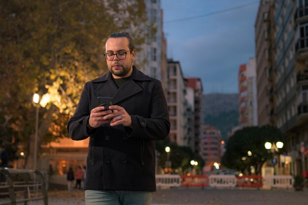 Homem anda e olha para o telefone na rua à noite