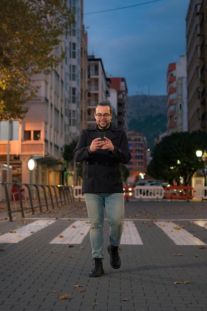 Homem anda e olha para o telefone na rua à noite