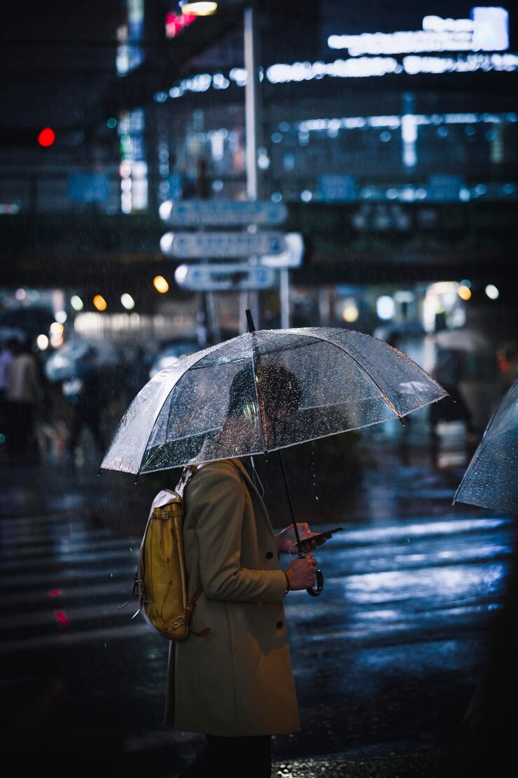 Homem andando com um guarda-chuva transparente em uma cidade à noite