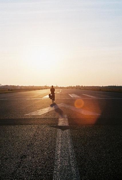 Homem andando de bicicleta na estrada contra o céu durante o pôr do sol