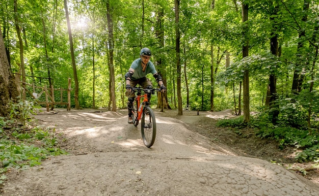 Homem andando de bicicleta na estrada da floresta à sombra de árvores altas