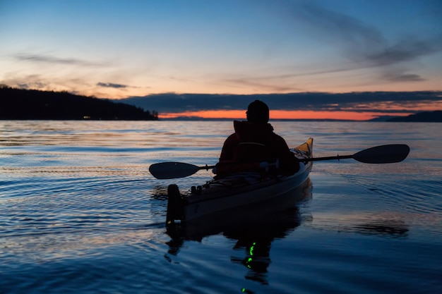 Homem andando de caiaque no mar durante um pôr do sol vibrante