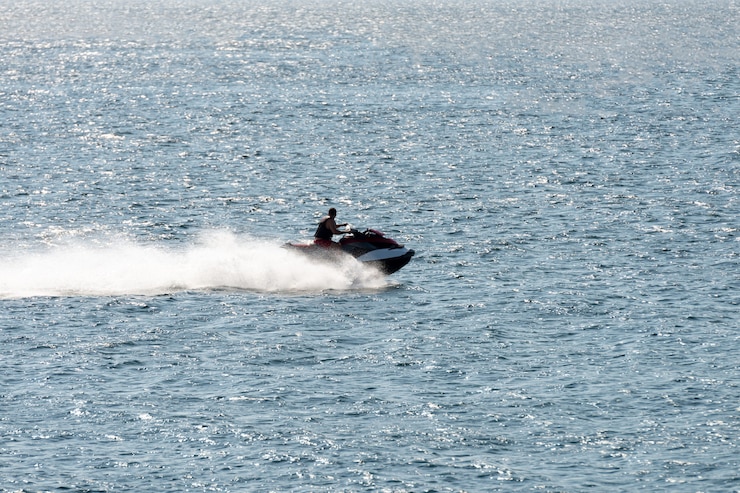 Foto homem andando de jet ski atirando em contraluz ao pôr do sol