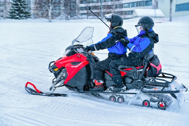 Homem andando de moto de neve e mulher com bastão de selfie tirando fotos de si mesmos no lago congelado no inverno Rovaniemi, Lapônia, Finlândia