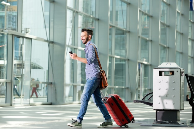 Homem andando no aeroporto com mala e telefone celular