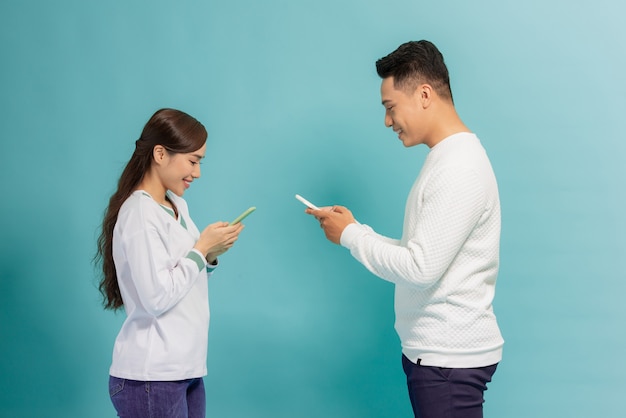 Homem animado e mulher falando segurando smartphones, olhando para o outro em pé sobre o azul.