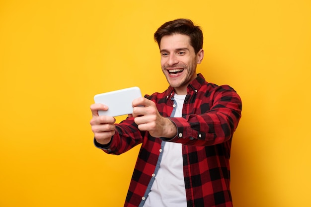 Homem animado jogando jogos para celular no fundo amarelo do estúdio
