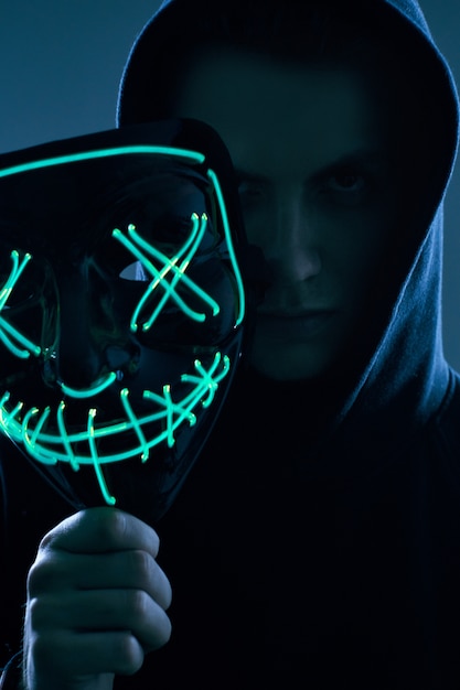 Foto homem anônimo de capuz preto, escondendo o rosto atrás de uma máscara de néon