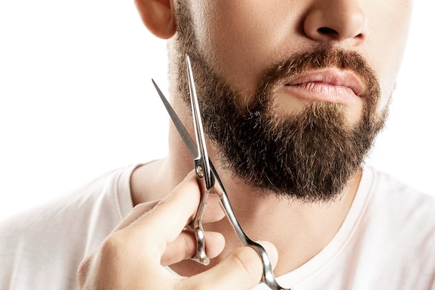 Homem aparando a barba com uma tesoura no fundo branco