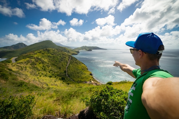 Foto homem apontando uma vista espetacular das montanhas e do mar azul com nuvens no fundo. conceito de férias e viagens.