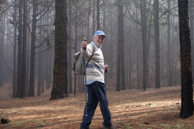 Homem aposentado sênior ativo e feliz com mochila caminhando na floresta da montanha em um dia nebuloso