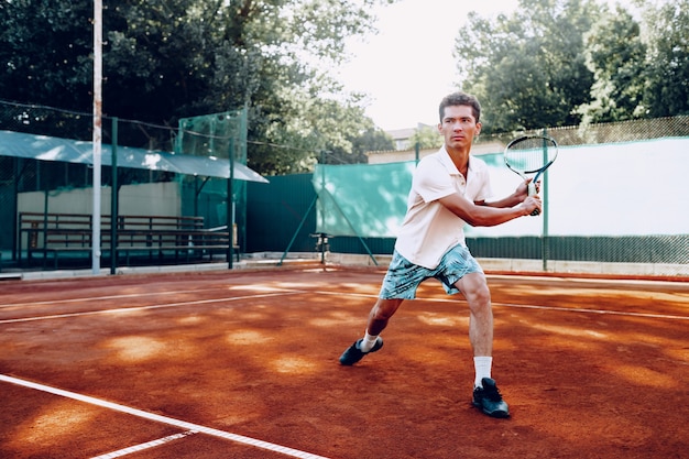 Homem apto joga tênis no campo de tênis pela manhã