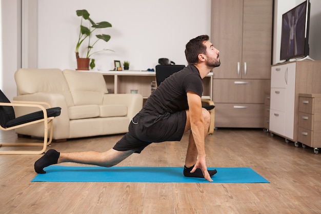Homem apto na casa dos 30 anos fazendo ioga em um colchão em sua casa. Estilo de vida esportivo saudável