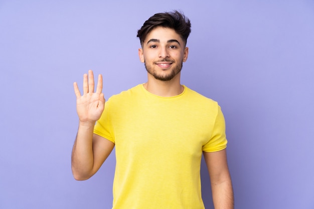 Homem árabe bonito saudando a parede isolada com a mão e expressão feliz