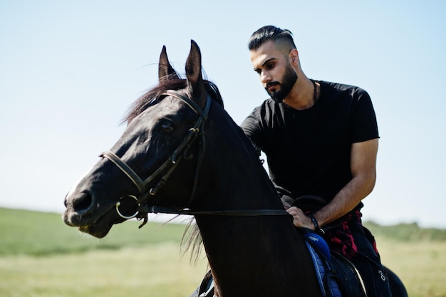 Homem árabe de barba alta usa cavalo árabe de passeio preto.