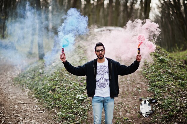 Homem árabe de estilo de rua em óculos segurar flare de mão com bomba de granada de fumaça vermelha e azul.