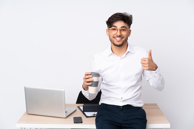 Homem árabe em um escritório na parede branca mostrando sinal ok e polegar para cima gesto