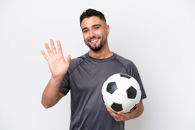 Homem árabe jovem jogador de futebol isolado no fundo branco saudando com a mão com expressão feliz