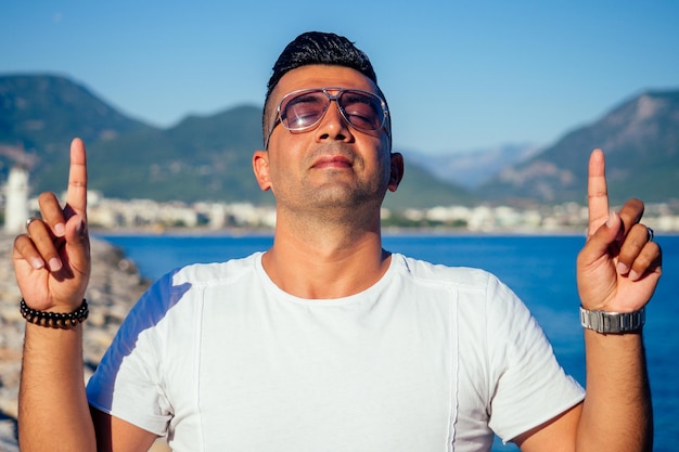 Homem árabe rico em moda usa óculos escuros e short branco posado contra o mar arábico