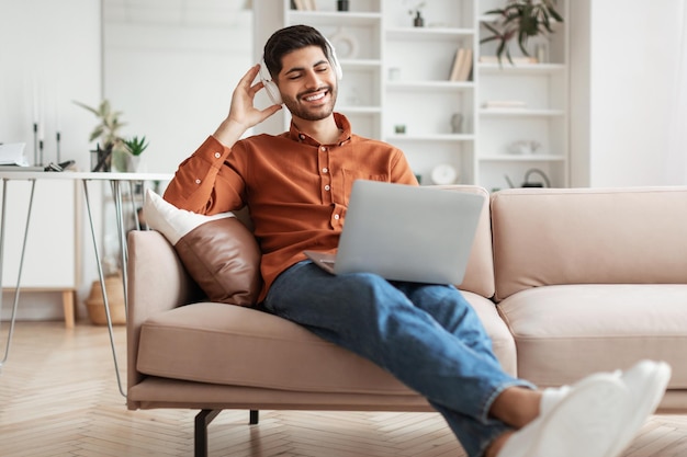 Homem árabe sorridente usando pc em casa ouvindo música