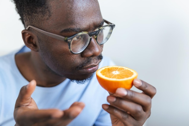 Homem aricano doente tentando sentir o cheiro de meia laranja fresca, tem sintomas de Covid-19, infecção pelo vírus corona - perda de olfato e paladar. Um dos principais sinais da doença.