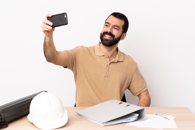 Homem arquiteto caucasiano com barba em uma mesa fazendo uma selfie.