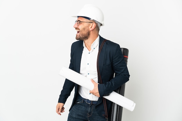 Homem arquiteto com capacete e segurando plantas isoladas no fundo branco rindo em posição lateral