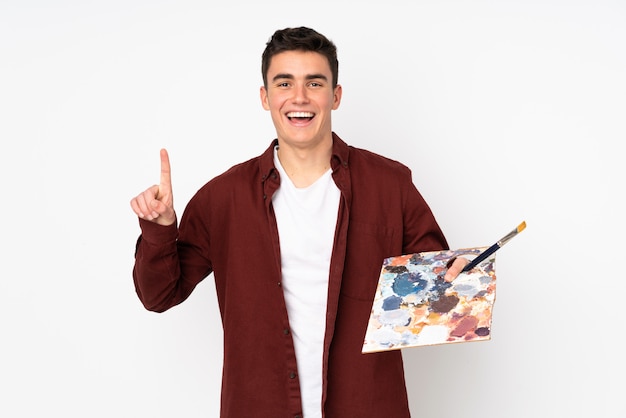 Homem artista adolescente segurando uma paleta na parede branca apontando para cima uma ótima idéia