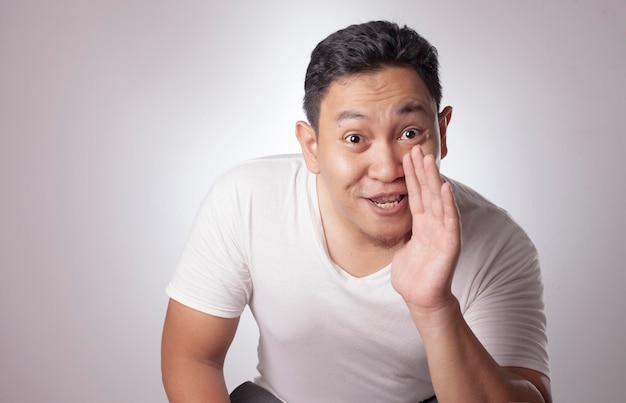 Homem asiático a falar em segredo a sussurrar atrás da mão na boca a contar segredo a alguém