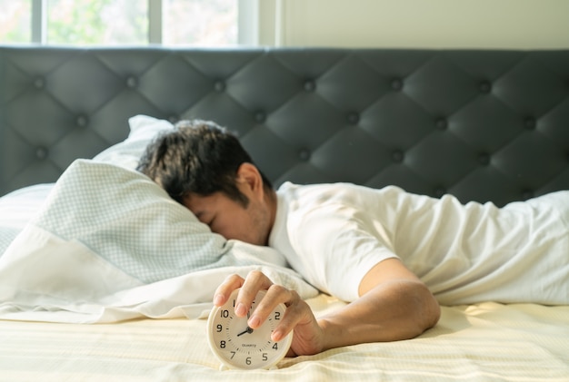 Homem asiático acorda de manhã e mão atingindo o despertador