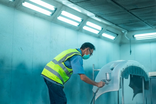 Homem asiático adulto está usando arma de pintura na oficina de pintura mecânica