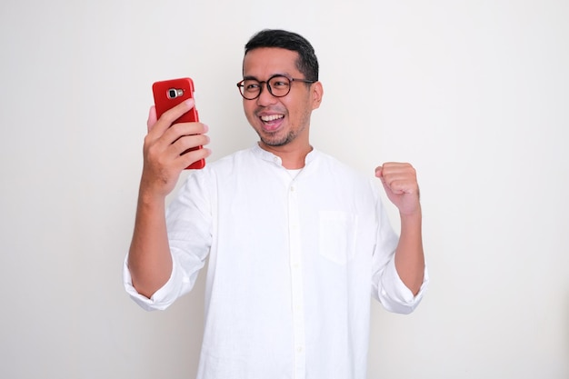 Homem asiático adulto mostrando expressão animada ao olhar para o celular