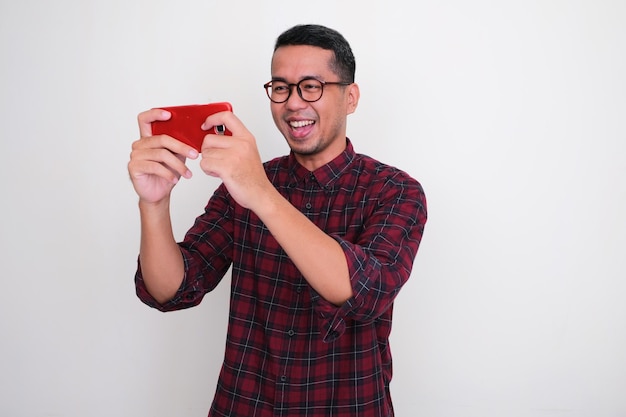 Homem asiático adulto mostrando expressão feliz ao jogar usando seu telefone celular