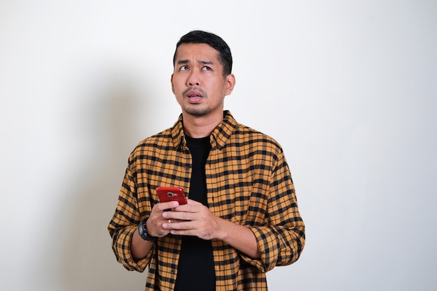 Foto homem asiático adulto pensa algo enquanto digita em seu telefone celular