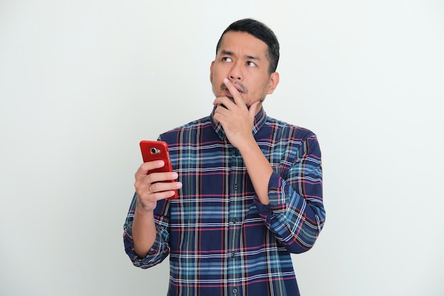Homem asiático adulto pensando em algo enquanto segura o celular